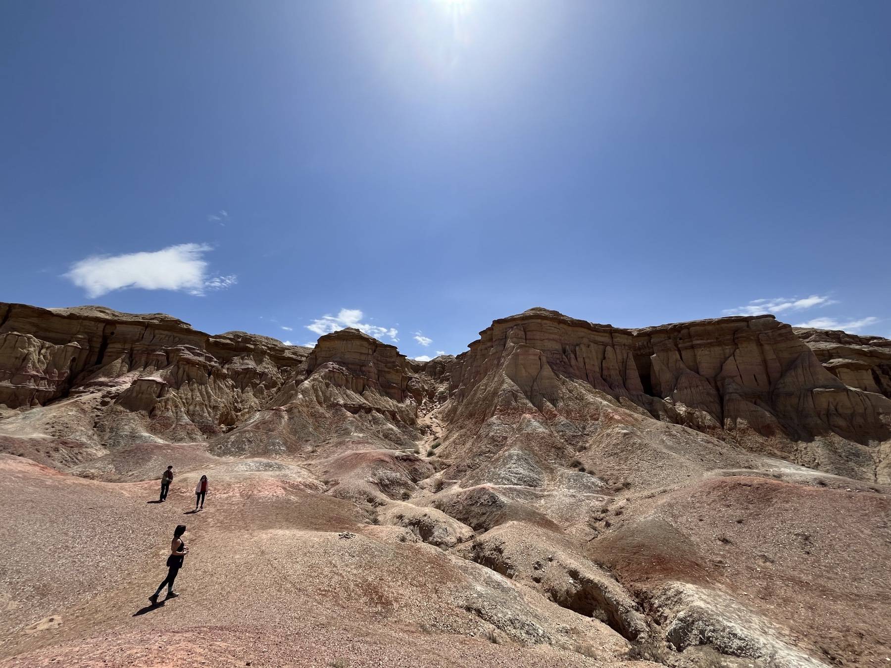 Hikers walking below eroded, layered cliffs in the Gobi Desert