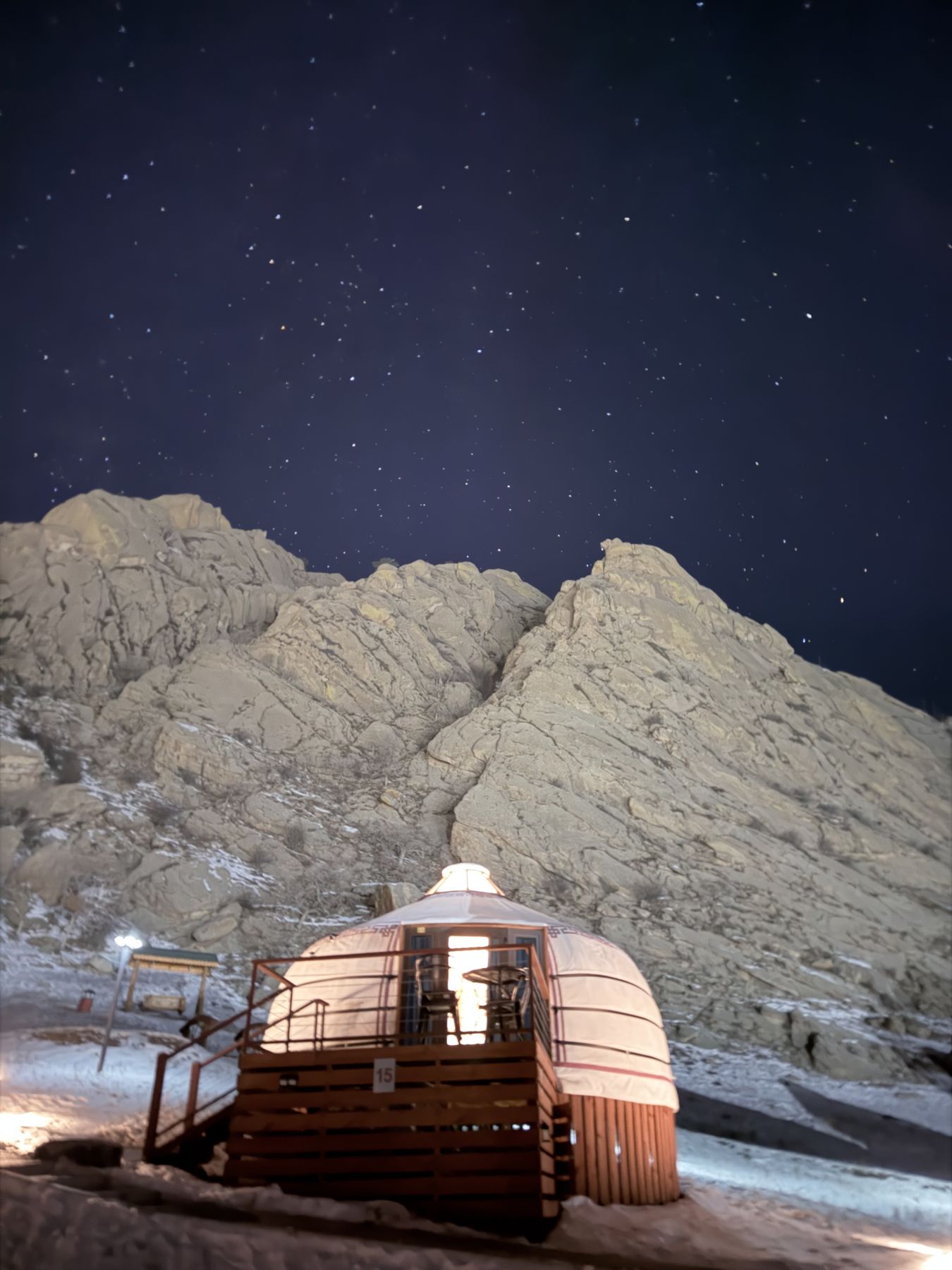A lit ger below snow-dusted granite rocks under a starry winter sky in Mongolia