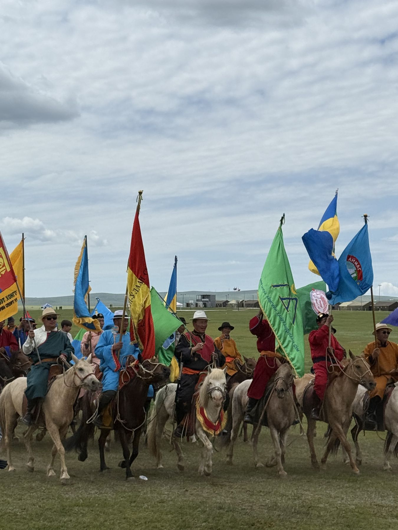 Riders in traditional Mongolian dress carrying flags on horseback during Naadam week, July 2026